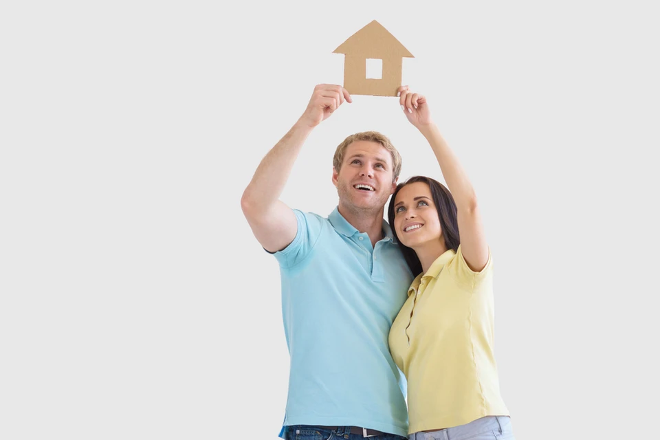 Couple souriant tenant ensemble une maquette de maison en carton au-dessus de leurs têtes, exprimant joie et accomplissement
