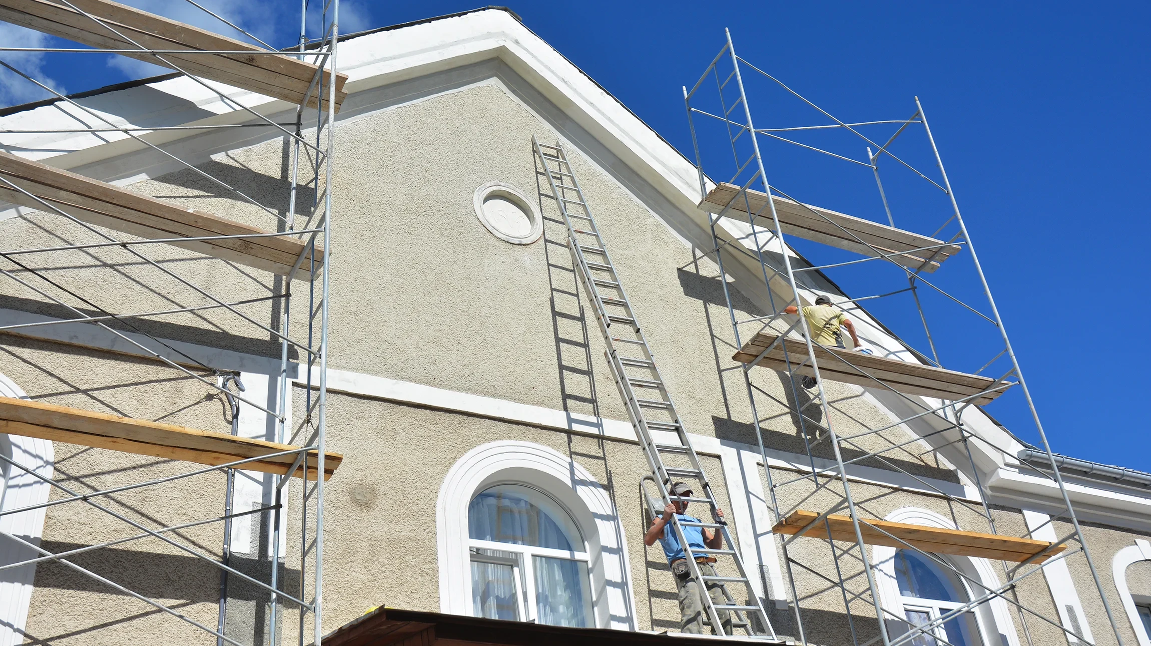 Chantier de rénovation extérieure avec ouvriers en vestes haute visibilité jaunes sur échafaudages métalliques