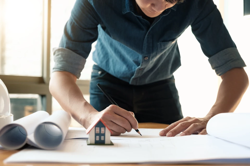 Chantier de construction extérieur avec homme en tenue de travail, casque de sécurité jaune, bras croisés devant bâtiments en construction